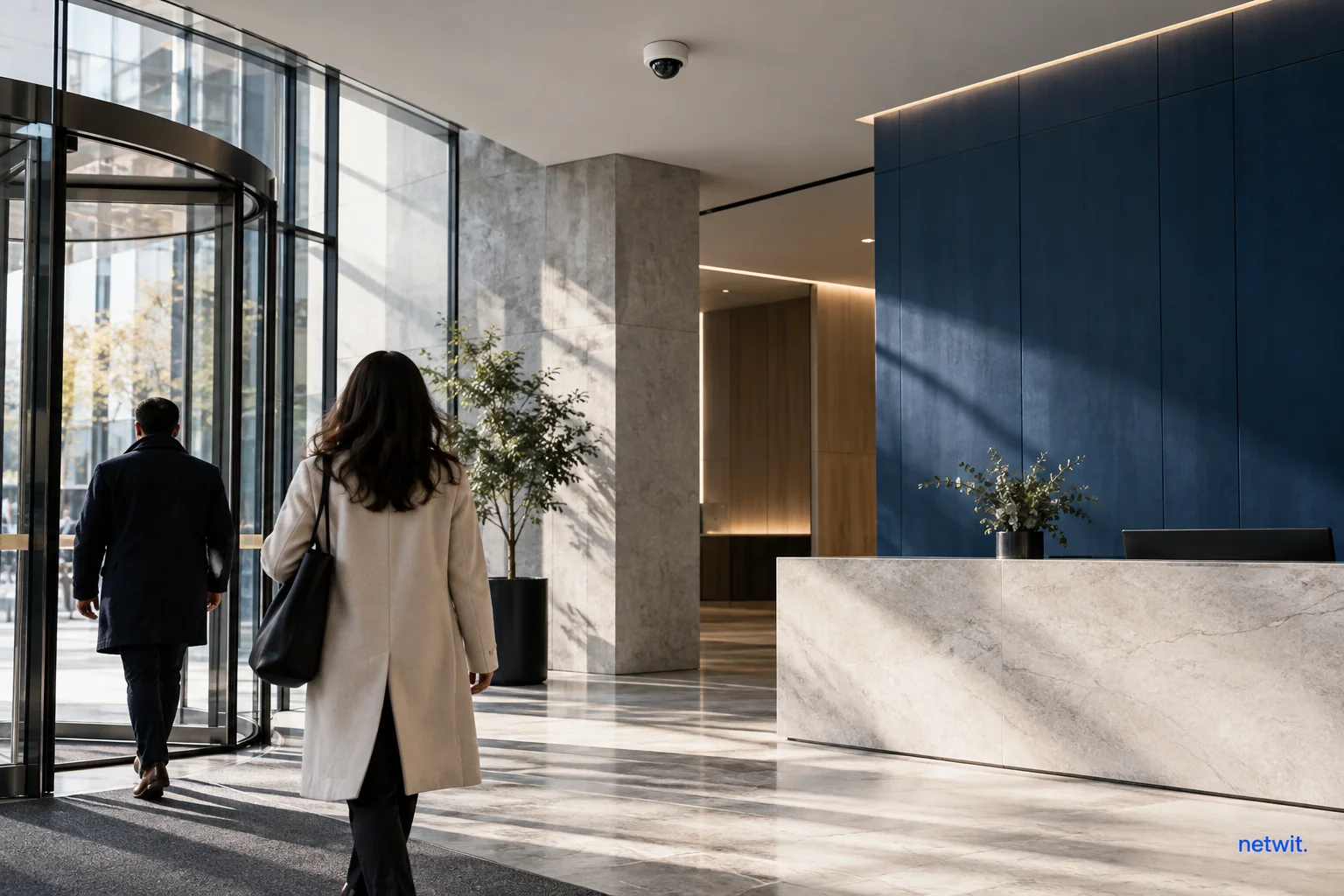 Anonymous visitors entering a contemporary office lobby beneath a small visible ceiling sensor, restrained architectural documentary composition.