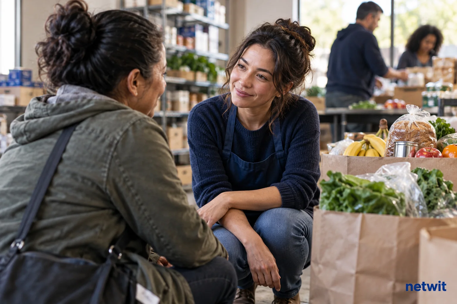 A community food pantry volunteer lowering a camera to listen to another adult at eye level, neatly packed groceries beside them, respectful dignified candid scene, no visible hardship spectacle..